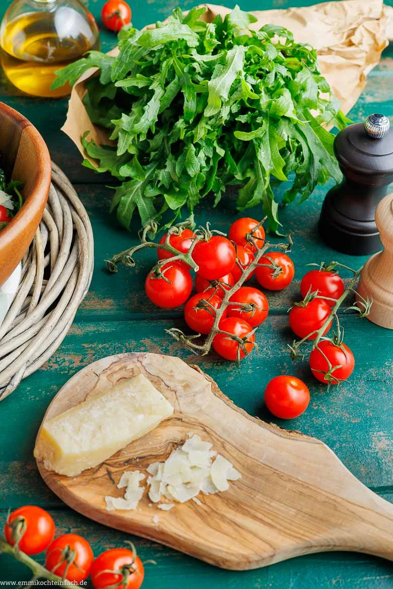 Frische Zutaten für Rucola-Salat: Rucola, Kirschtomaten und gehobelter Parmesan